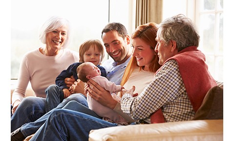 Multi Generation Family Sitting On Sofa With Newborn Baby